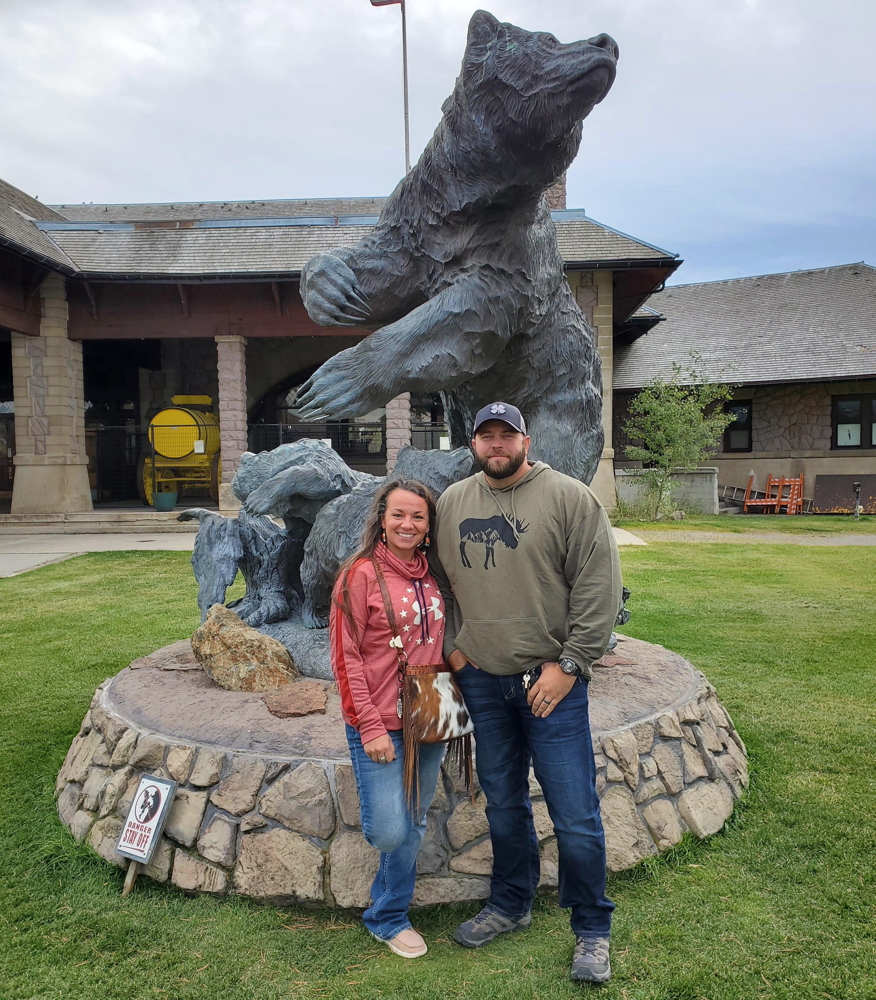 Beef tallow maker and her husband standing next to a bear statue in an outdoor setting