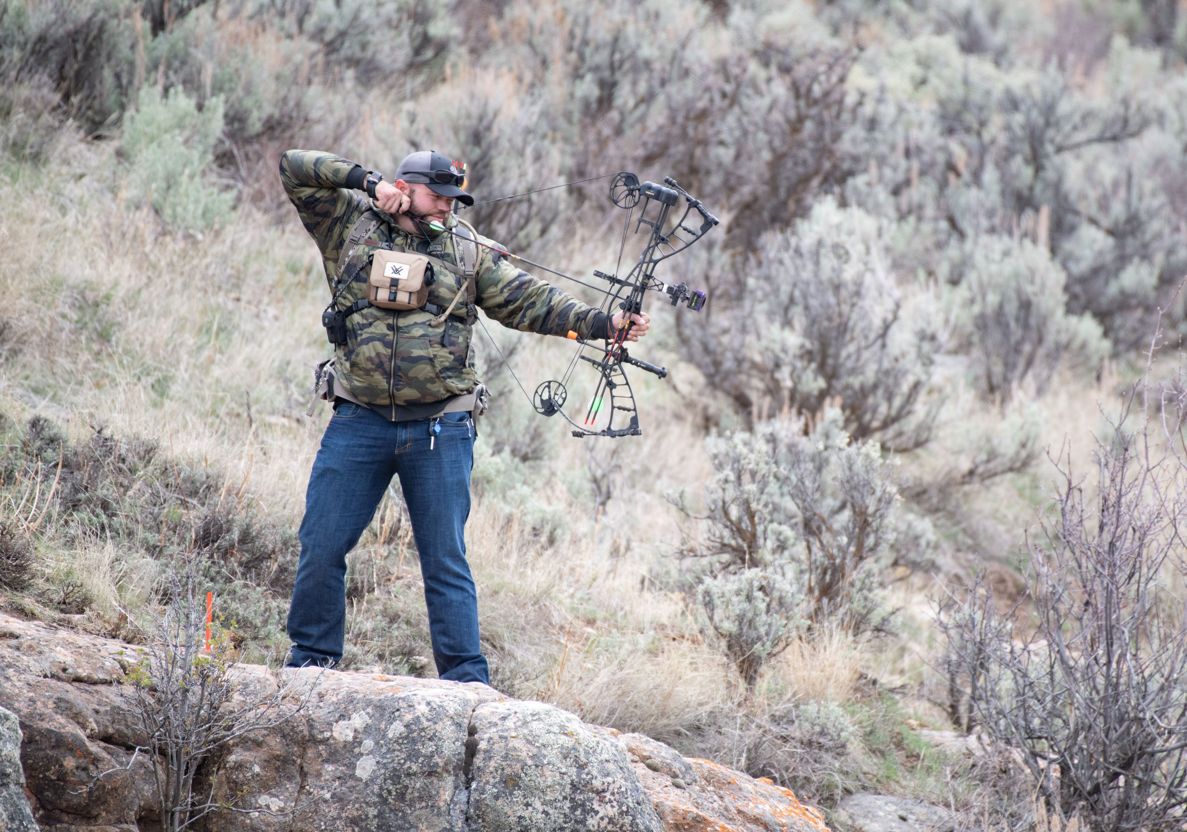 Beef tallow maker's husband holding his bow and arrow on the side of a mountain.